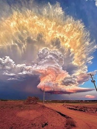 a large cloud is seen over a dirt road